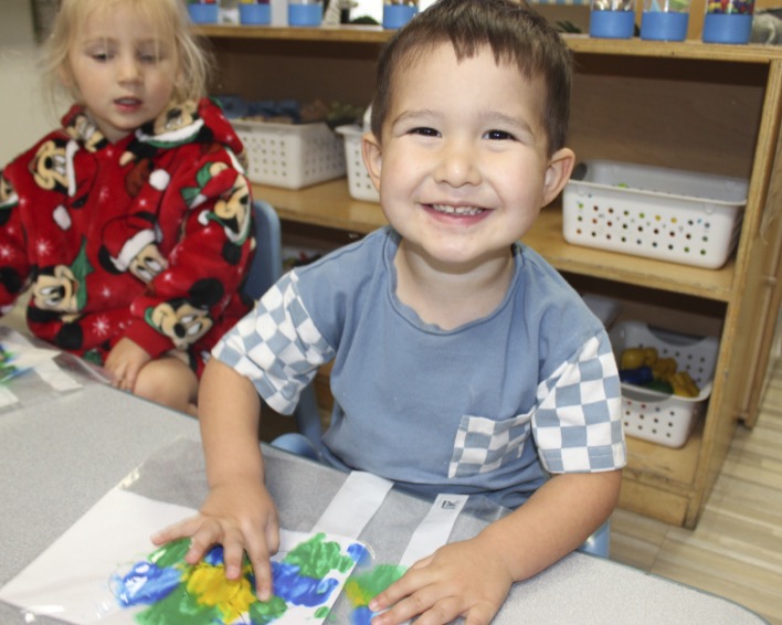 Smiling child finger painting in a classroom