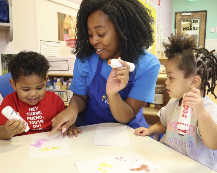 Adult and two children dot painting at a table in a classroom
