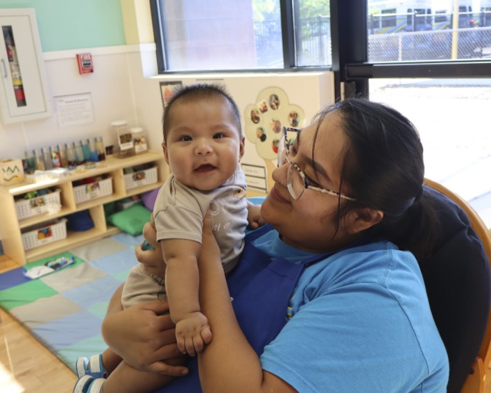 Adult person holding a smiling infant in a classroom