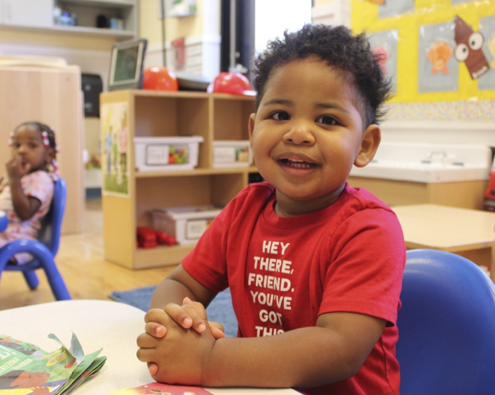 Smiling child at a table in a classroom with another child in the background