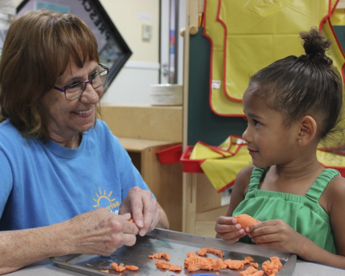 Adult and child playing with orange modeling clay at a table