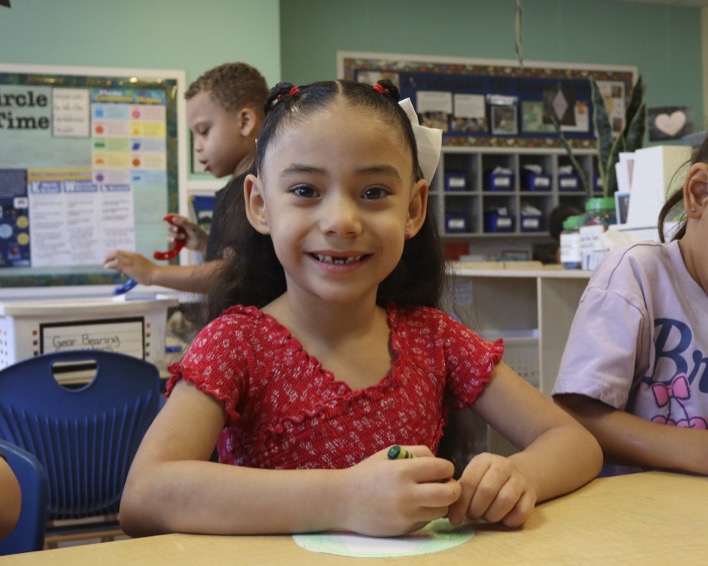 Child coloring at a table with other children in a classroom