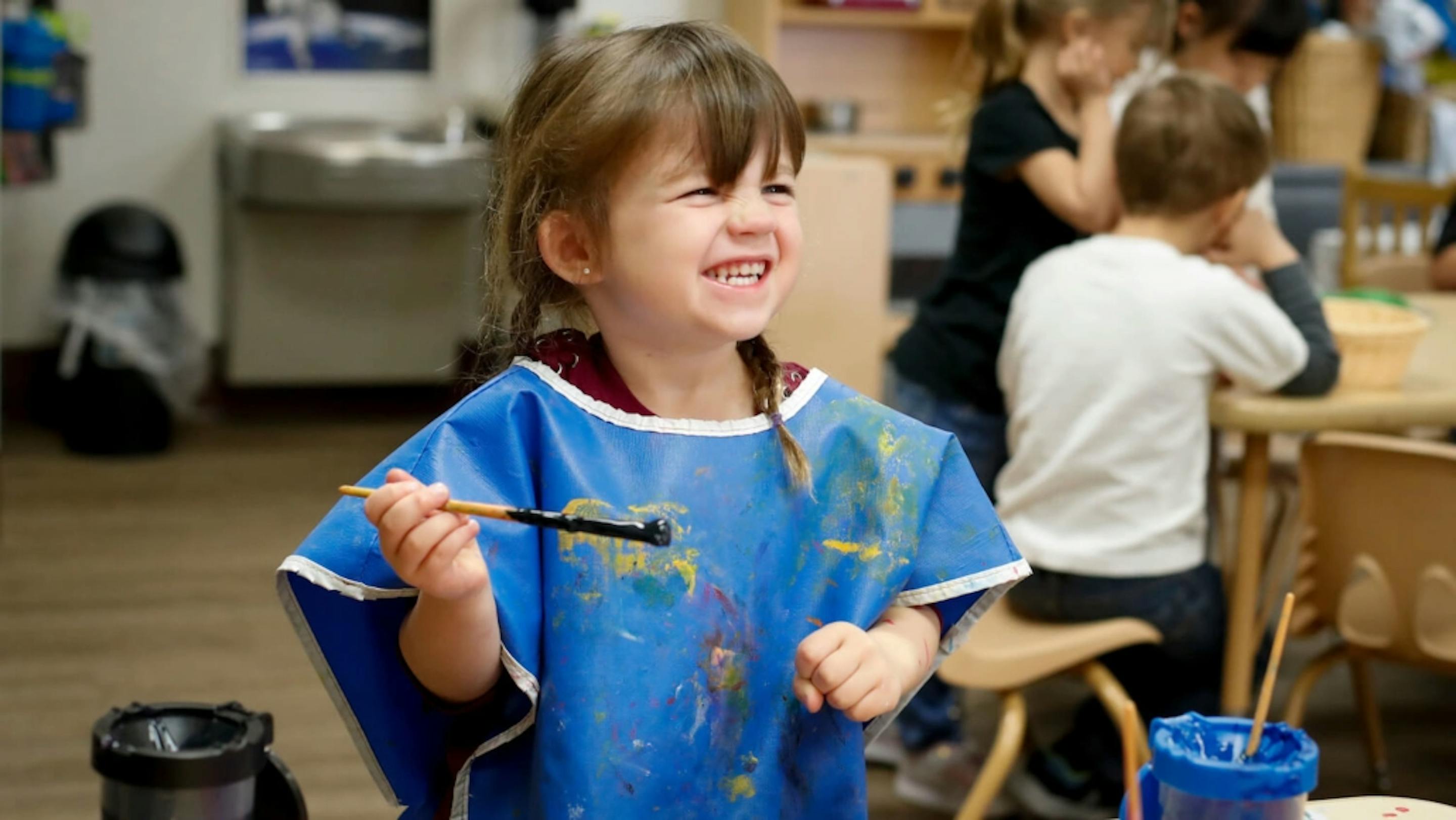 Child in a blue smock holding a paintbrush
