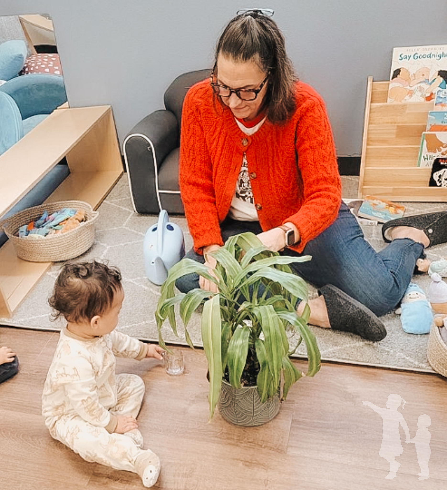 Person in red cardigan tending to a plant while a child watches