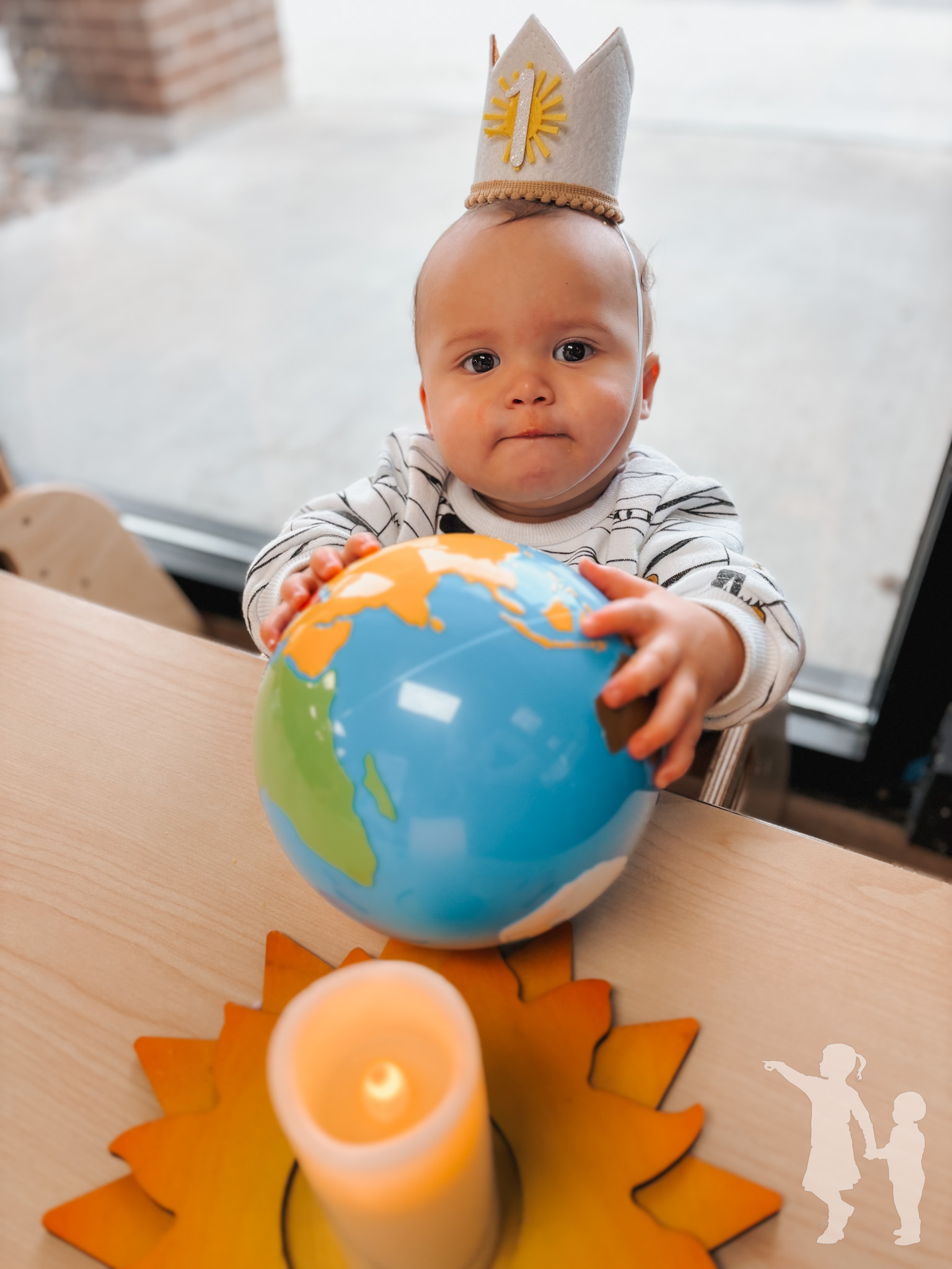 Child wearing a '1' crown, holding a globe, with a candle on a sun coaster