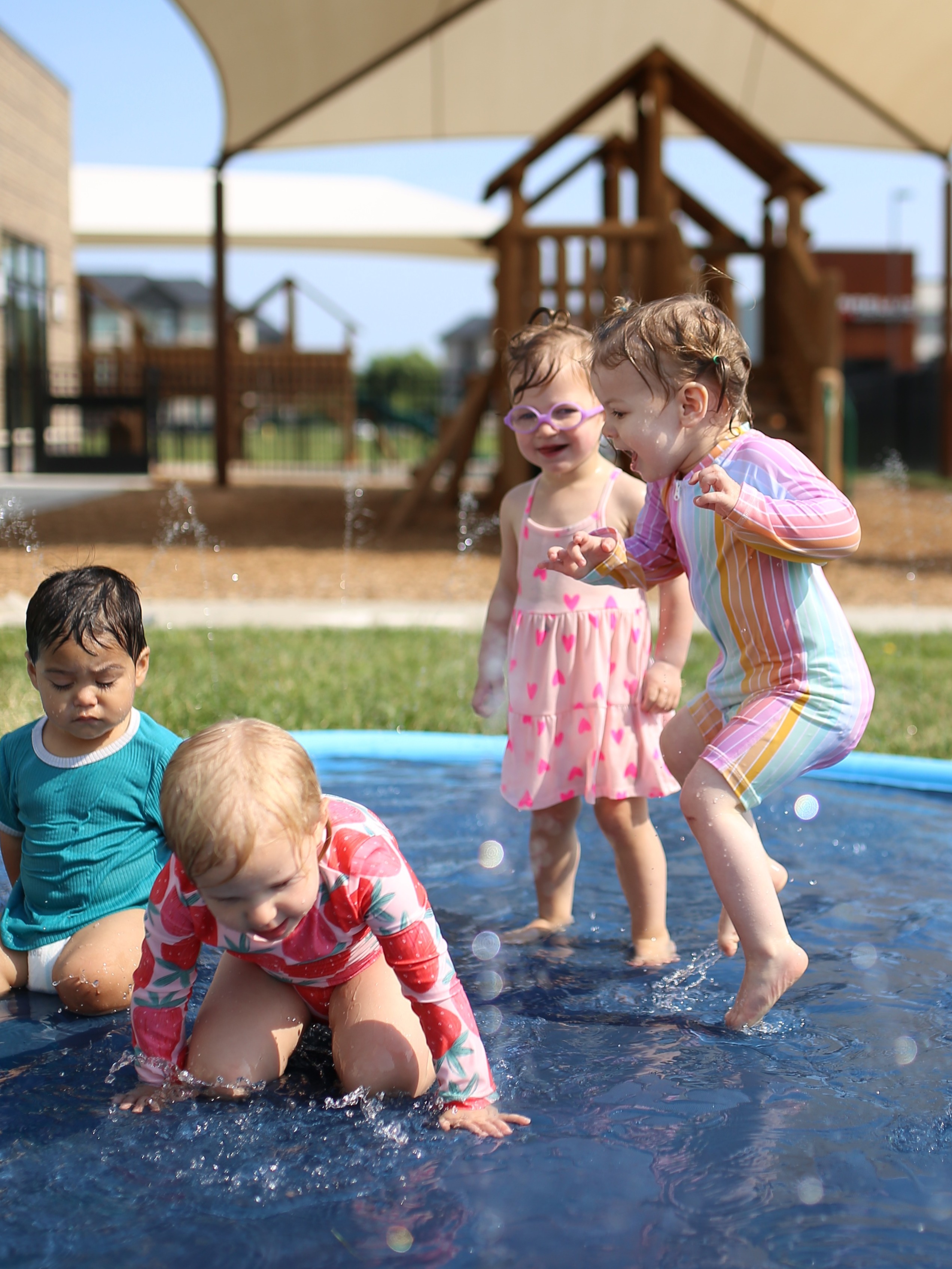 Four children playing in a shallow pool of water outdoors