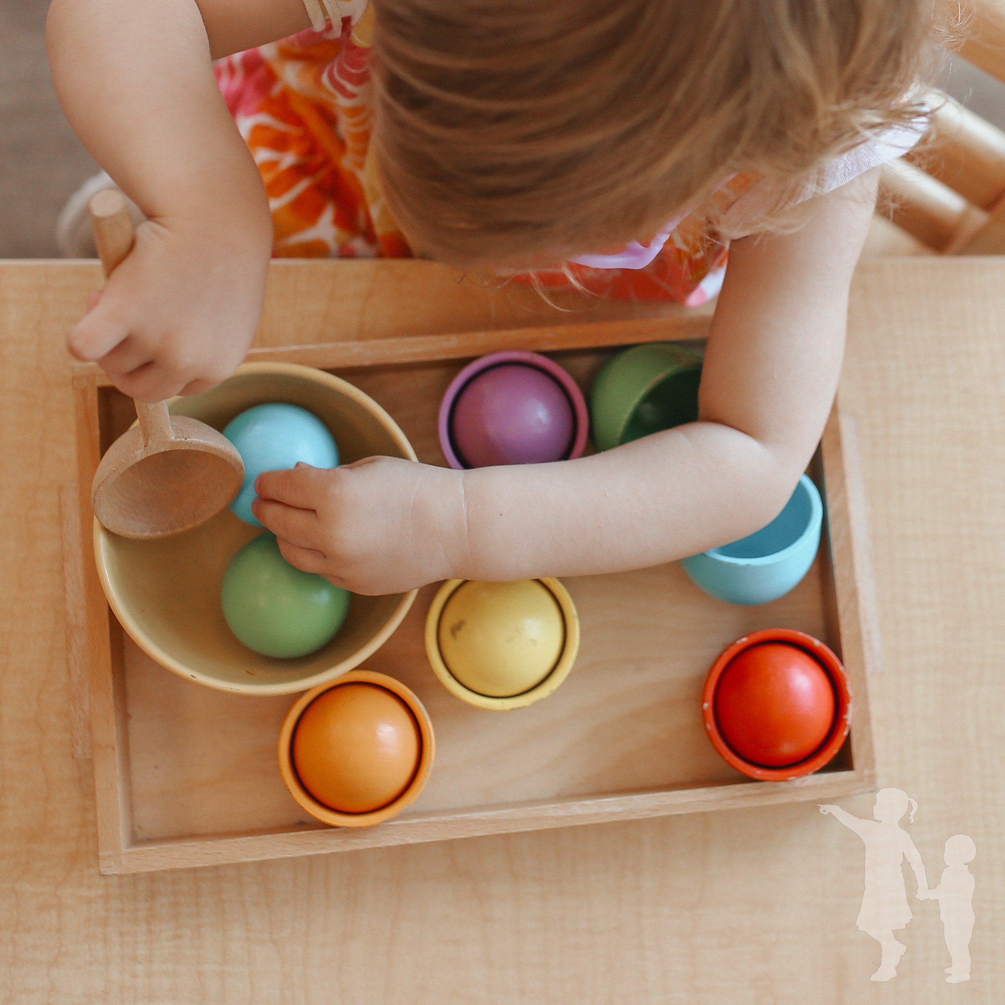 Child playing with colorful Montessori balls and cups in a wooden tray