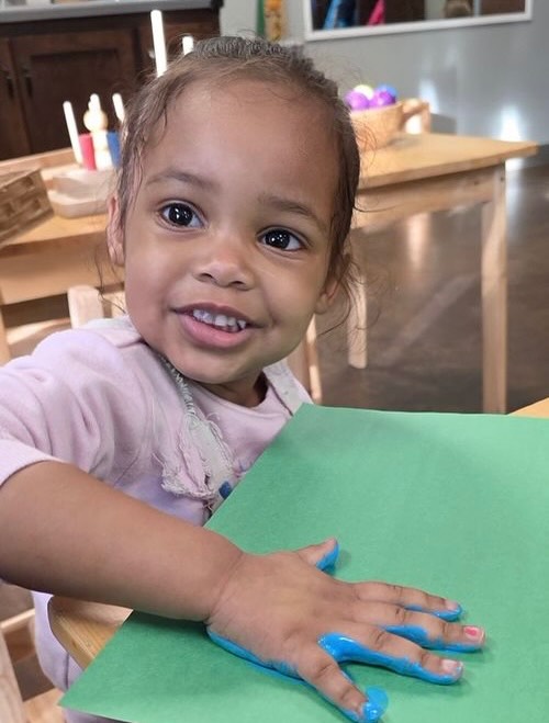 Child with blue paint on hand over green paper