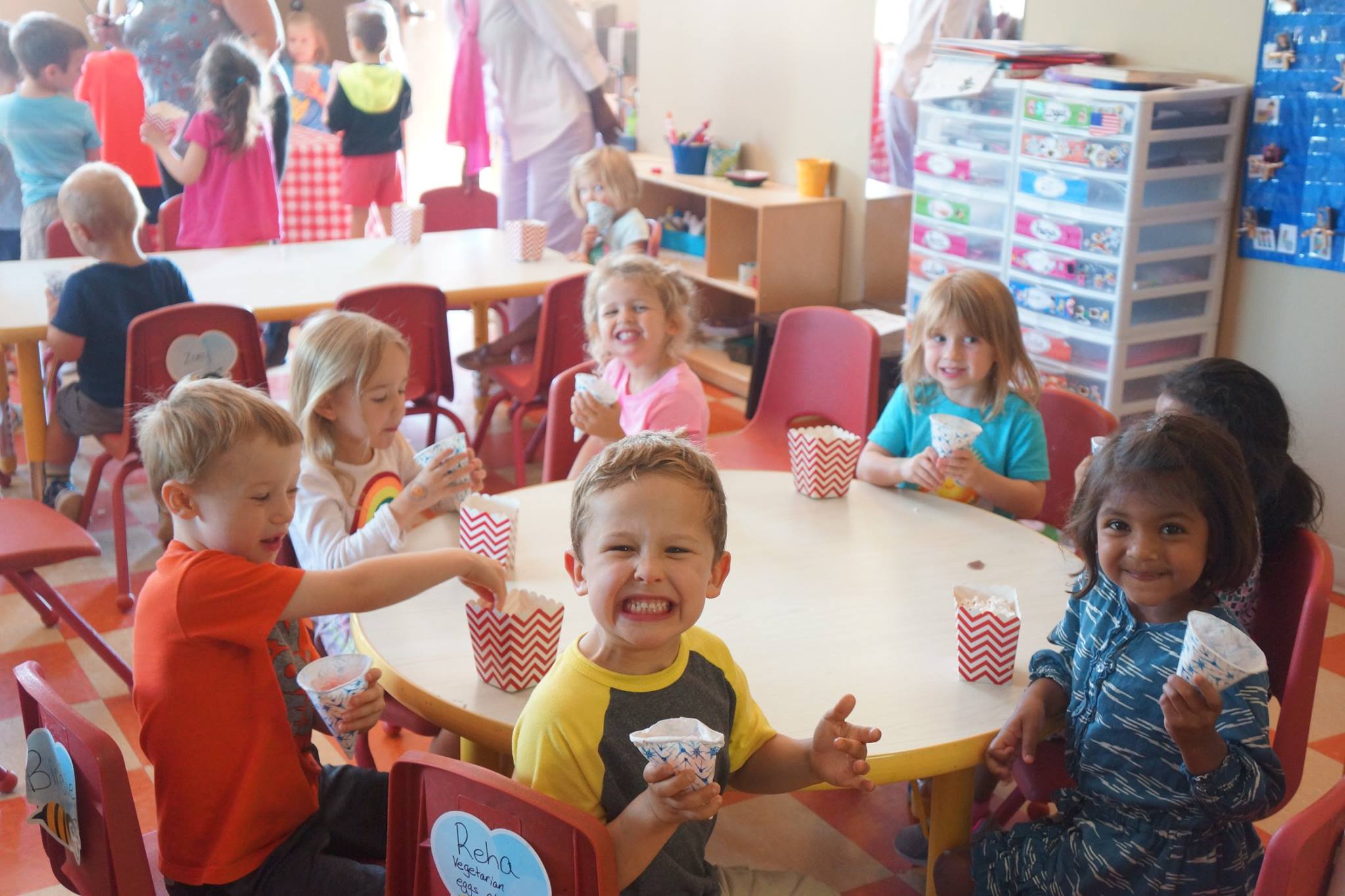 Children sitting around tables in a classroom, holding cups and small popcorn bags