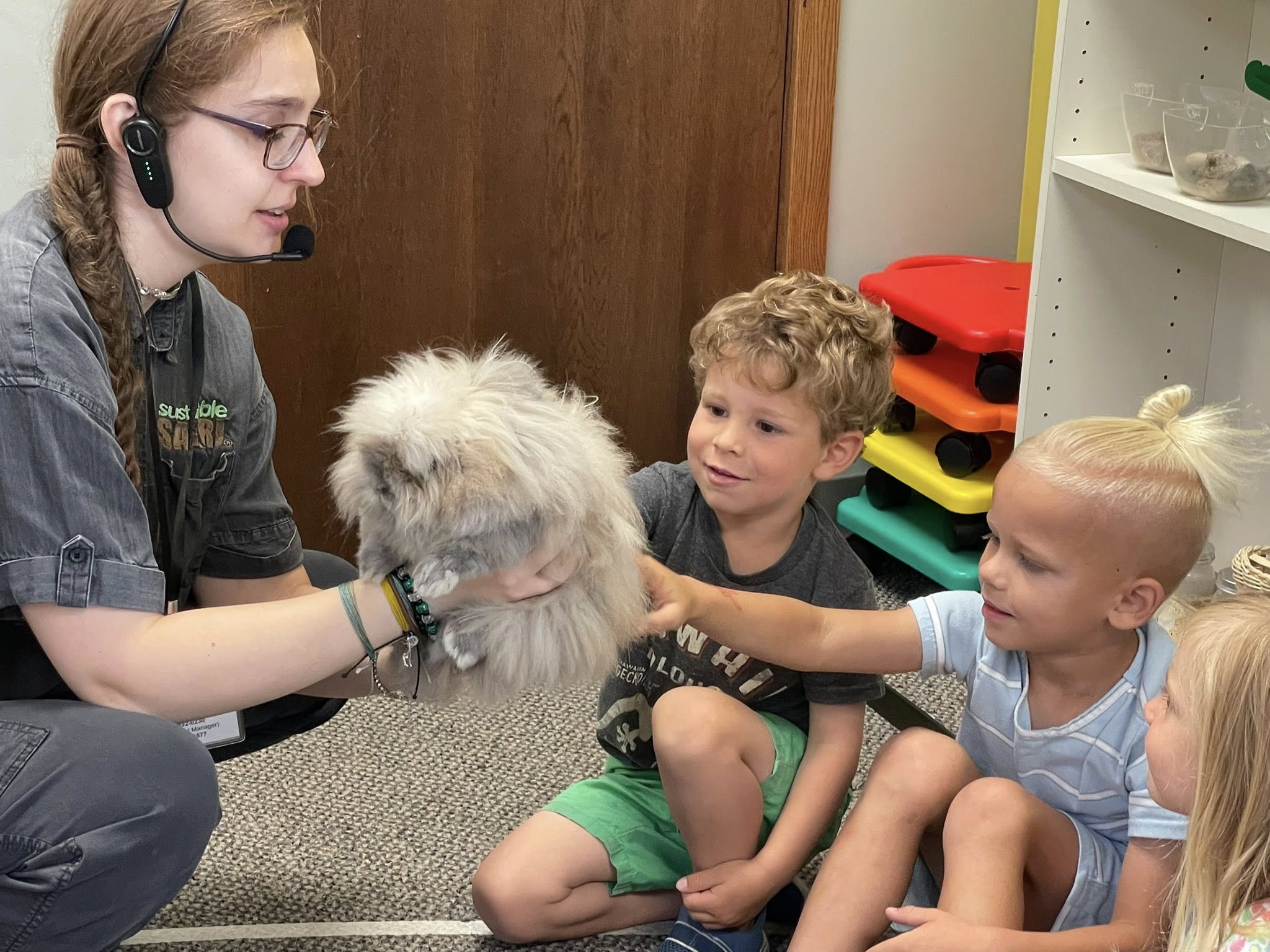 Person holding a fluffy animal while two children reach out to touch it