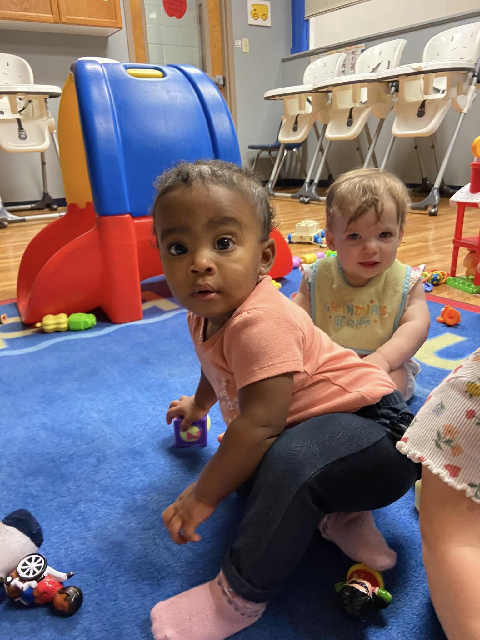 Two children playing on a blue mat in a classroom