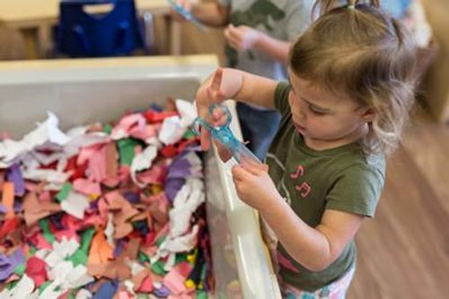 Child holding scissors over a bin of colorful fabric scraps