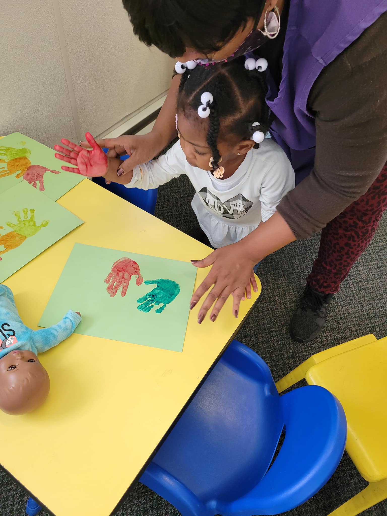 Person helping a child make handprints on paper