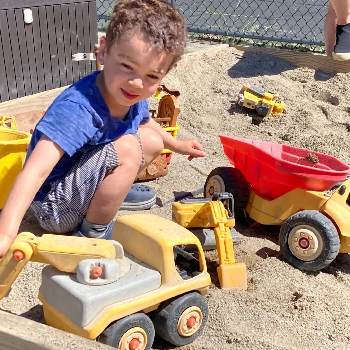 Child playing in a sandbox with toy construction vehicles