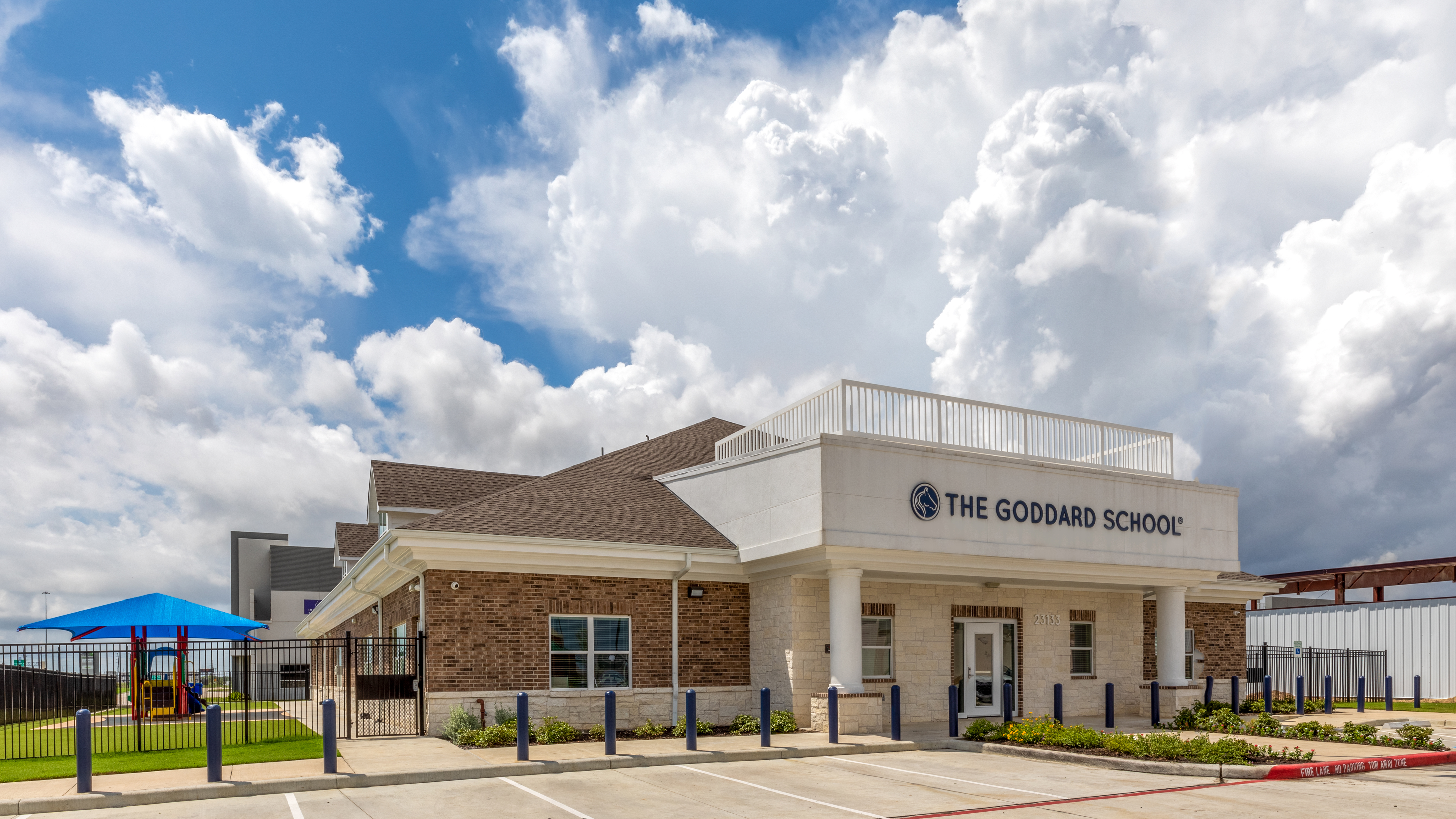 The Goddard School building exterior with a playground under a blue canopy