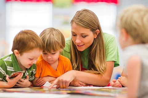 Person pointing to a book with two children looking on