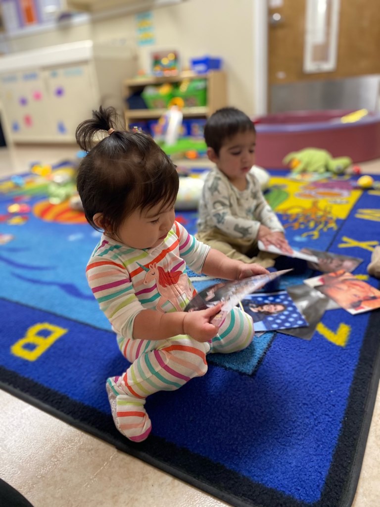 Two children sitting on a rug looking at pictures
