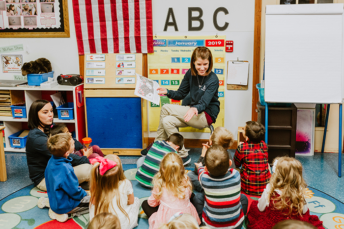Two adults reading to a group of children in a classroom
