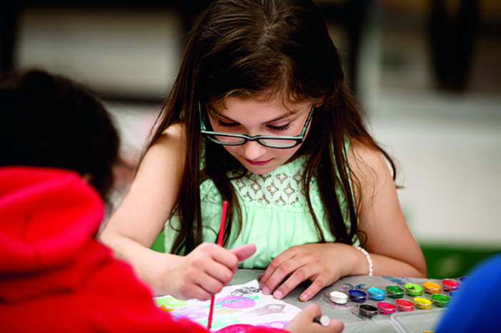 Child in glasses painting with watercolors