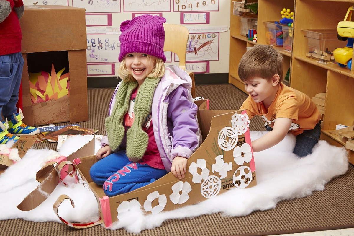 Two children playing with cardboard cutouts and cotton batting in a classroom