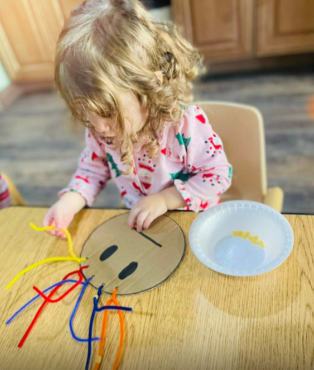 Child playing with pipe cleaners and a cardboard face