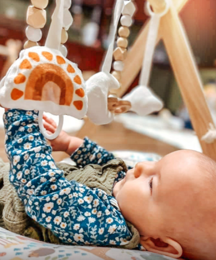 Child reaching for a rainbow toy on a play gym