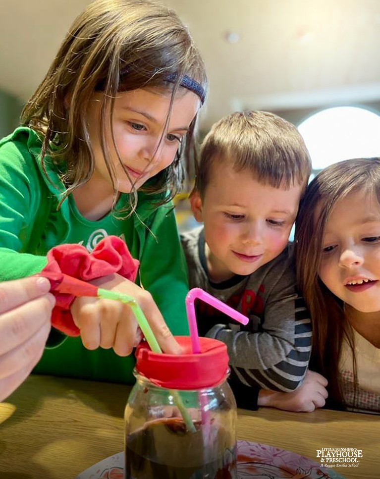 Three children looking at a jar with straws