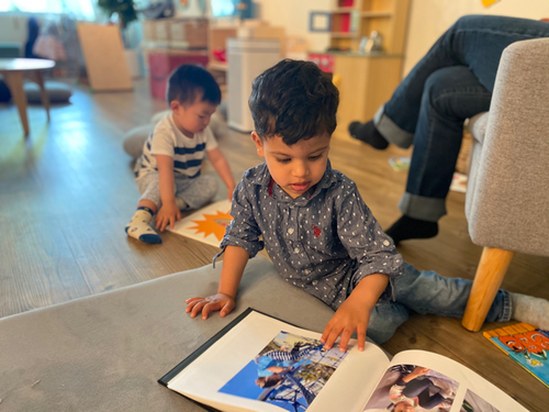 Child on floor looking at open book, another child in background