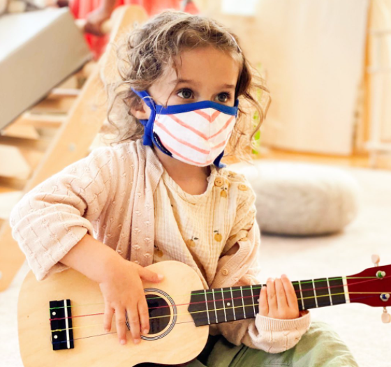 Child wearing a face mask and playing a ukulele
