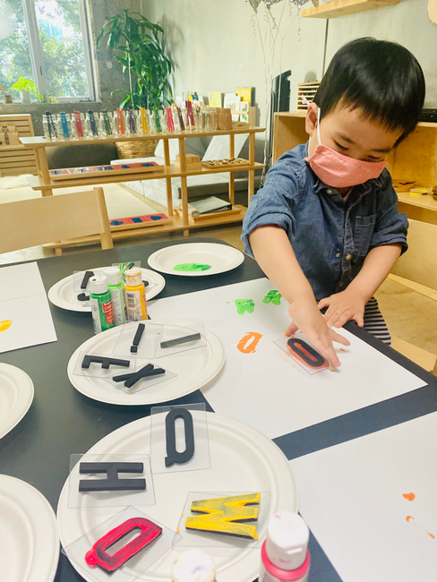 Child in a mask doing an art activity with letter stamps