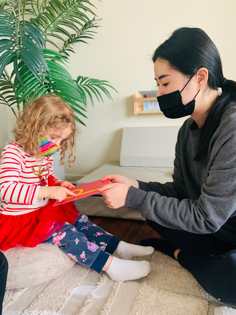 Adult and child in masks looking at a red book together